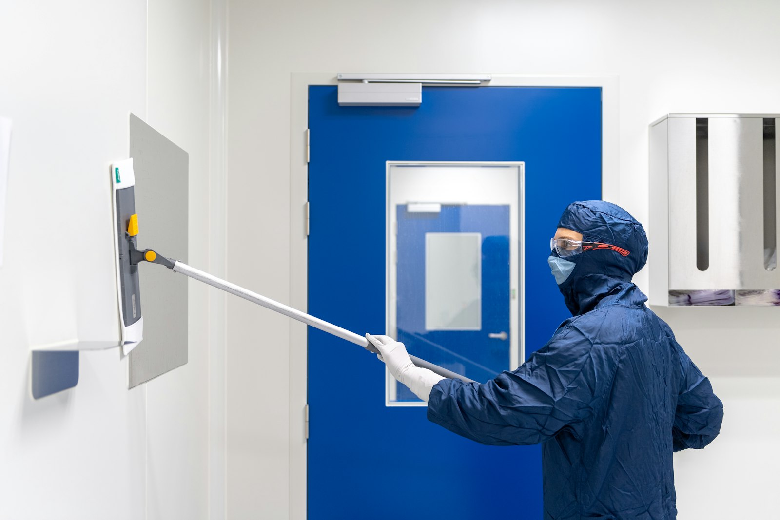 Technician cleaning a controlled laboratory wall and access panel